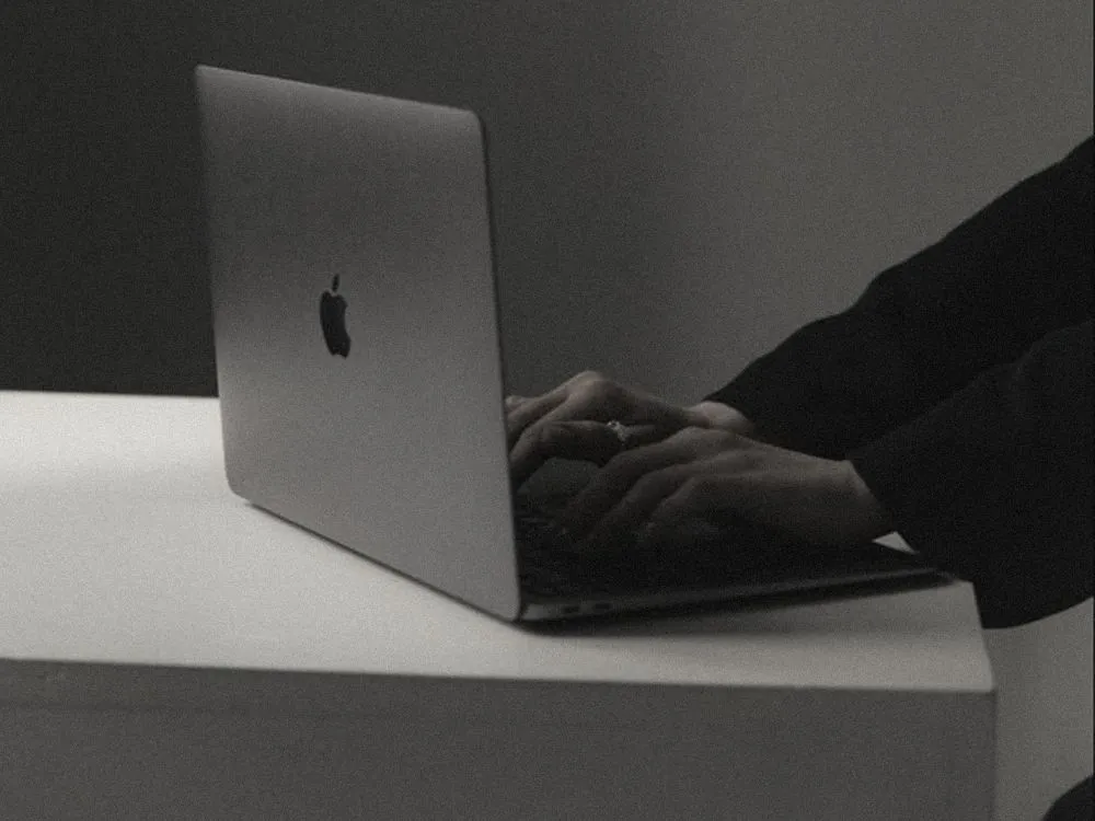 Hands typing on a silver laptop on a white surface