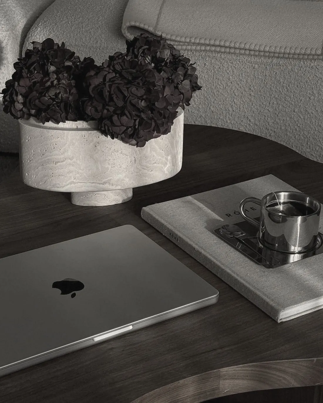 A closed laptop beside dried hydrangeas and a coffee on a timber table
