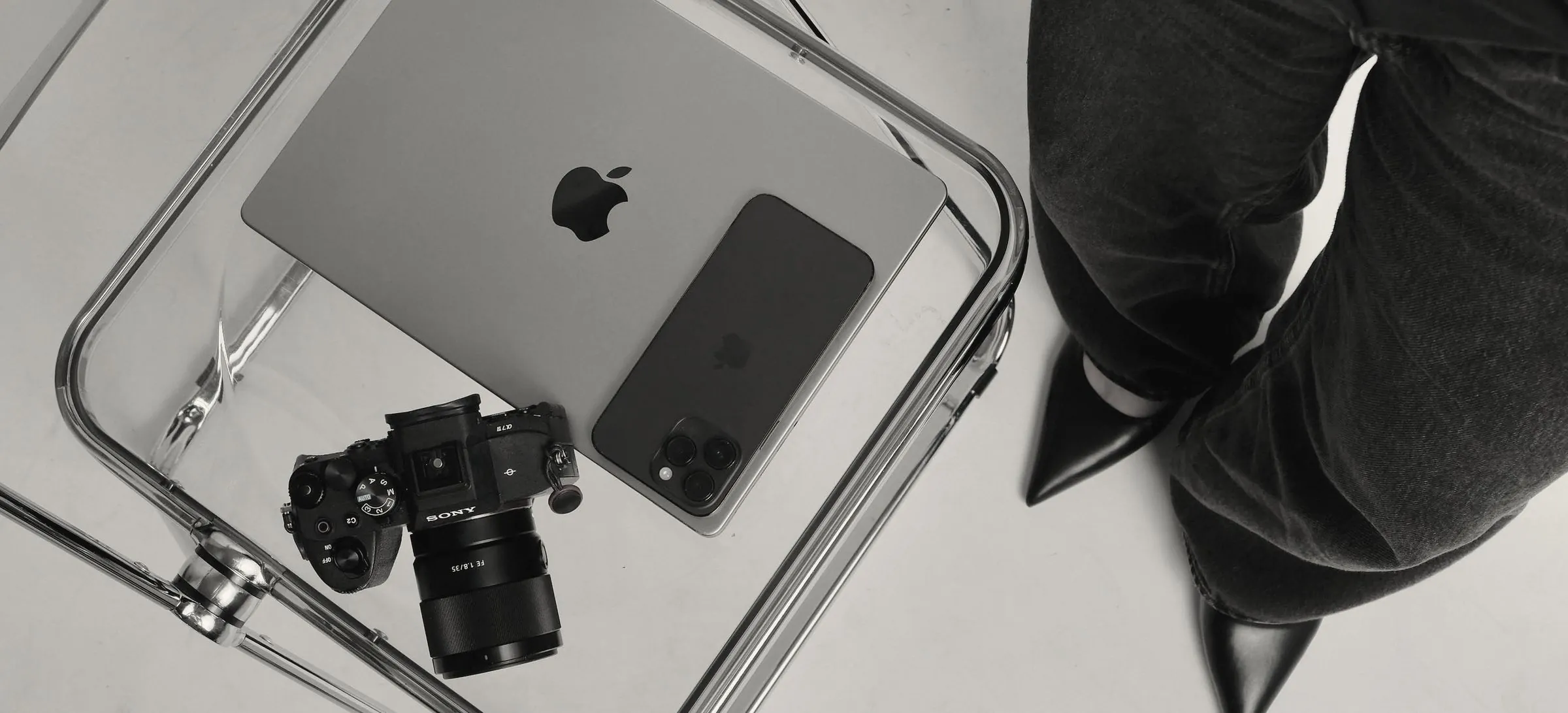 A laptop, phone and camera on a clear acrylic chair beside someone dressed in black