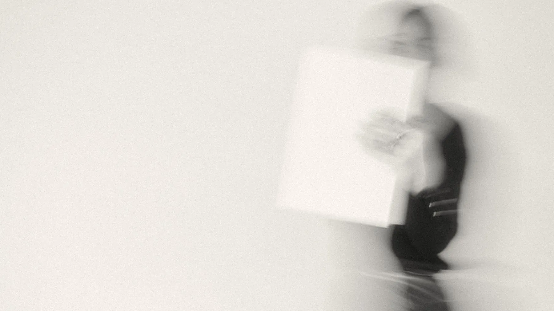A blurred figure in black carrying a white folder across a bright room
