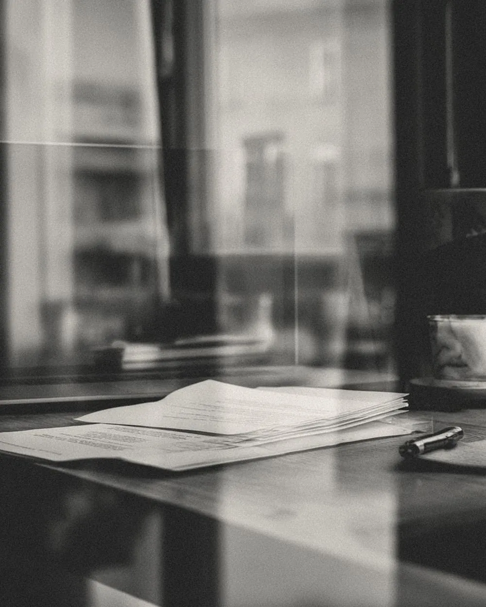 A desk by a window with papers and a pen in soft light