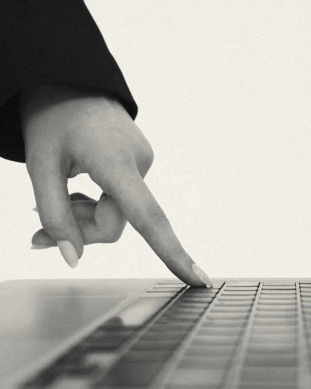 A fingertip pressing a key on a silver laptop